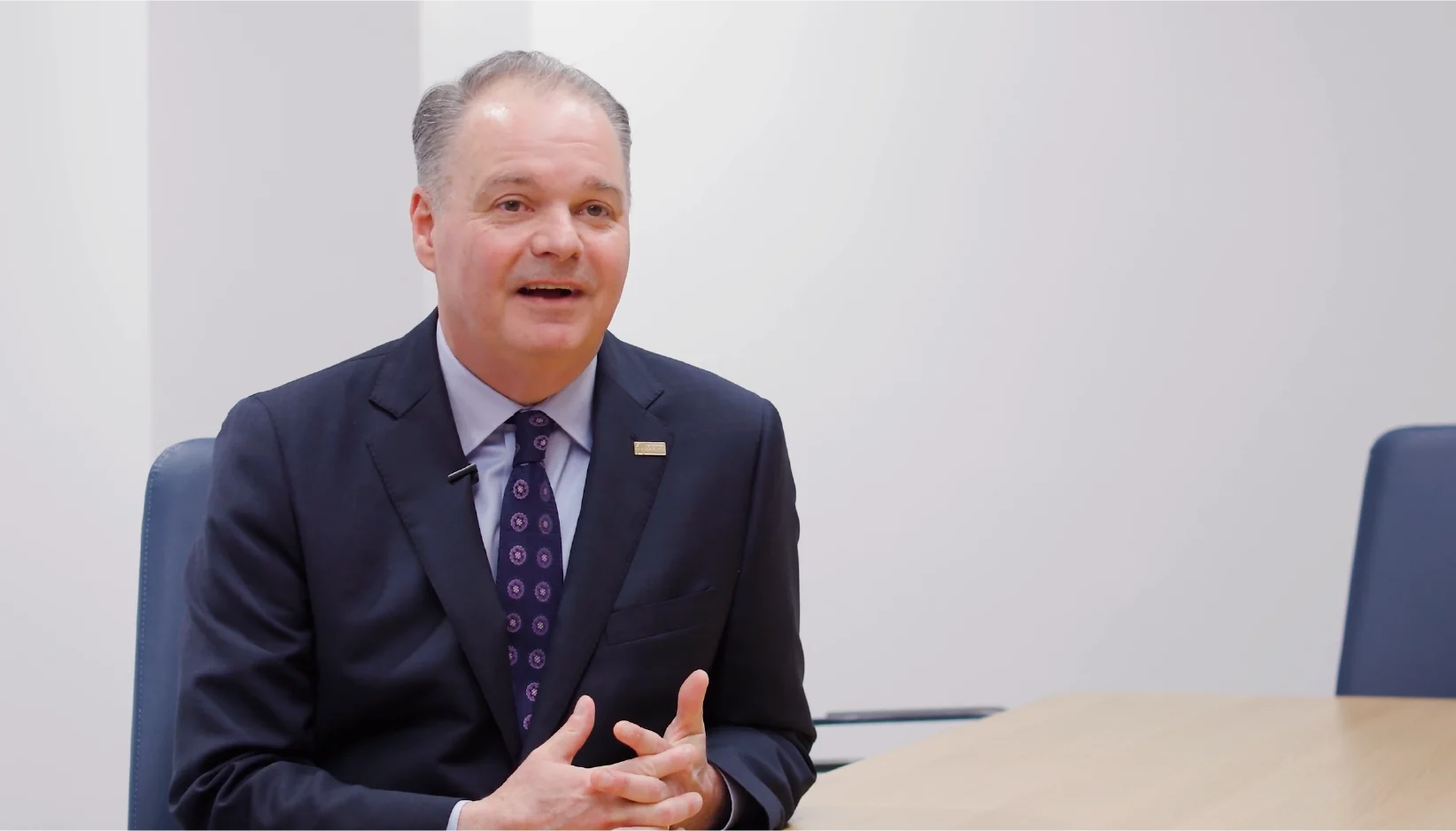 A man in a suit and tie at a conference table being interviewed